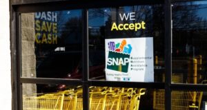 SNAP en Alabama sufrirá recortes por nueva ley federal Letrero oficial del programa SNAP en la ventana de un supermercado con carritos de compra amarillos en Alabama.