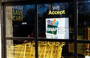 SNAP en Alabama sufrirá recortes por nueva ley federal Letrero oficial del programa SNAP en la ventana de un supermercado con carritos de compra amarillos en Alabama.