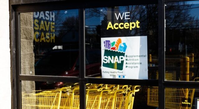 SNAP en Alabama sufrirá recortes por nueva ley federal Letrero oficial del programa SNAP en la ventana de un supermercado con carritos de compra amarillos en Alabama.