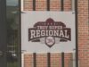 Súper Regionales: Troy aplasta a Little Rock en el Juego 1 Lona oficial con el logotipo del torneo Troy Super Regional 2026 colgada en una reja de ladrillos.