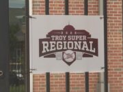 Súper Regionales: Troy aplasta a Little Rock en el Juego 1 Lona oficial con el logotipo del torneo Troy Super Regional 2026 colgada en una reja de ladrillos.