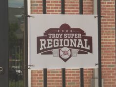 Súper Regionales: Troy aplasta a Little Rock en el Juego 1 Lona oficial con el logotipo del torneo Troy Super Regional 2026 colgada en una reja de ladrillos.