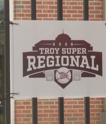 Súper Regionales: Troy aplasta a Little Rock en el Juego 1 Lona oficial con el logotipo del torneo Troy Super Regional 2026 colgada en una reja de ladrillos.