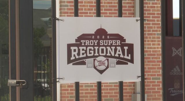 Súper Regionales: Troy aplasta a Little Rock en el Juego 1 Lona oficial con el logotipo del torneo Troy Super Regional 2026 colgada en una reja de ladrillos.