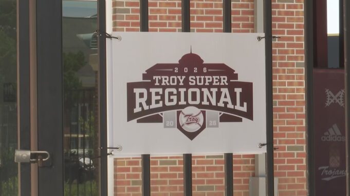 Súper Regionales: Troy aplasta a Little Rock en el Juego 1 Lona oficial con el logotipo del torneo Troy Super Regional 2026 colgada en una reja de ladrillos.