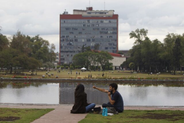 Crisis en mayor universidad de México abre debate sobre futuro de admisiones en era de IA Estudiantes sentados frente al espejo de agua con el edificio de Rectoría de la UNAM al fondo en México.