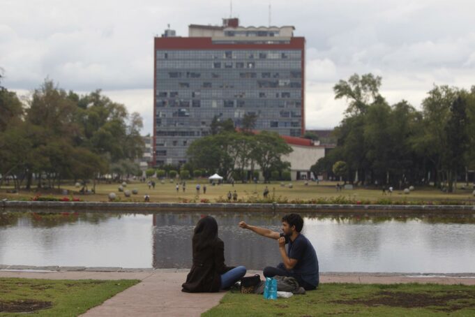 Examen UNAM 2026 bajo revisión por sospecha de uso de IA Estudiantes sentados frente al espejo de agua con el edificio de Rectoría de la UNAM al fondo en México.