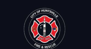Huntsville aprueba terreno para nueva estación de bomberos Escudo oficial de Huntsville Fire and Rescue con la figura de un cohete espacial sobre fondo negro.