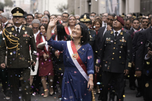 Keiko Fujimori sonríe y saluda con la banda presidencial de Perú rodeada de oficiales militares y confeti.