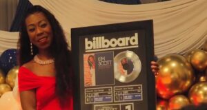 Kim Scott alcanza nuevo éxito número uno en Billboard La flautista Kim Scott sostiene un cuadro conmemorativo del número uno de Billboard por su canción Hide and Seek.