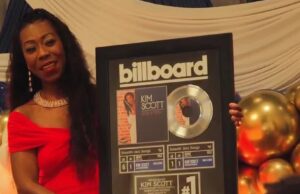 Kim Scott alcanza nuevo éxito número uno en Billboard La flautista Kim Scott sostiene un cuadro conmemorativo del número uno de Billboard por su canción Hide and Seek.