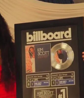 Kim Scott alcanza nuevo éxito número uno en Billboard La flautista Kim Scott sostiene un cuadro conmemorativo del número uno de Billboard por su canción Hide and Seek.