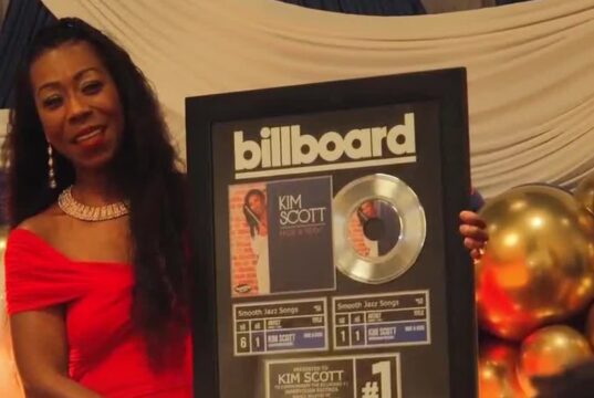Kim Scott alcanza nuevo éxito número uno en Billboard La flautista Kim Scott sostiene un cuadro conmemorativo del número uno de Billboard por su canción Hide and Seek.