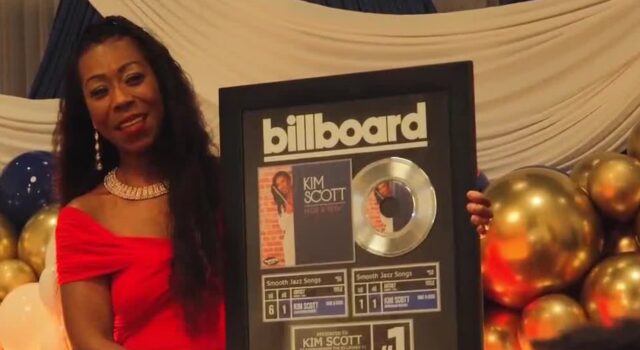 Kim Scott alcanza nuevo éxito número uno en Billboard La flautista Kim Scott sostiene un cuadro conmemorativo del número uno de Billboard por su canción Hide and Seek.