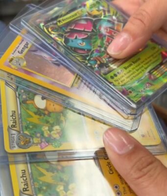 Alabama sufre ola de robos de valiosas cartas de Pokémon Manos sosteniendo cartas coleccionables de Pokémon en fundas protectoras como Raichu y Gengar en una tienda de Alabama.