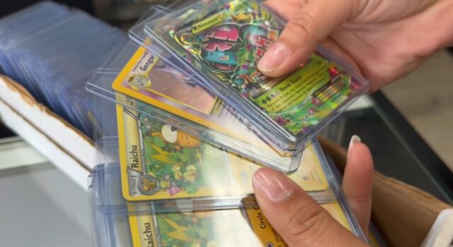 Alabama sufre ola de robos de valiosas cartas de Pokémon Manos sosteniendo cartas coleccionables de Pokémon en fundas protectoras como Raichu y Gengar en una tienda de Alabama.