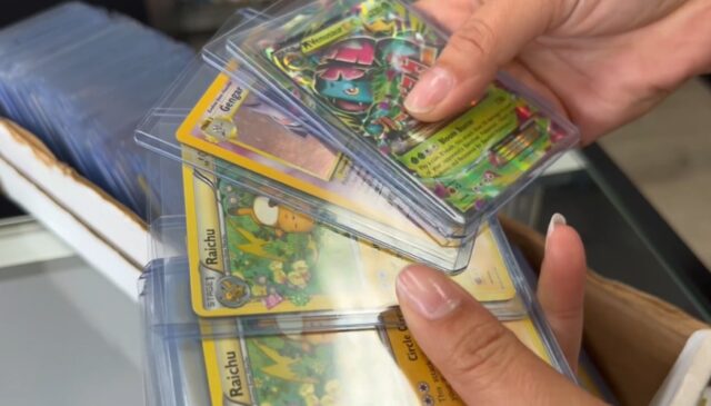 Manos sosteniendo cartas coleccionables de Pokémon en fundas protectoras como Raichu y Gengar en una tienda de Alabama.