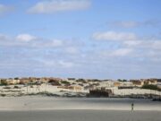Piura registra temperaturas récord por El Niño Costero Persona camina por un terreno desértico de Piura con viviendas rústicas bajo un cielo despejado por El Niño Costero.