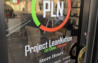 Project Lean Nation llega a Homewood con nutrición Fachada de Project Lean Nation en Homewood con su logotipo PLN y horarios de atención en la puerta de vidrio.