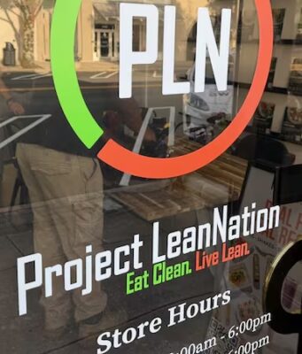 Project Lean Nation llega a Homewood con nutrición Fachada de Project Lean Nation en Homewood con su logotipo PLN y horarios de atención en la puerta de vidrio.