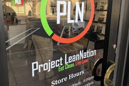 Project Lean Nation llega a Homewood con nutrición Fachada de Project Lean Nation en Homewood con su logotipo PLN y horarios de atención en la puerta de vidrio.