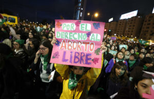 Protestas en Chile contra ley de latidos fetales y aborto Manifestante sostiene un cartel rosa sobre el aborto libre durante una marcha nocturna en Chile.