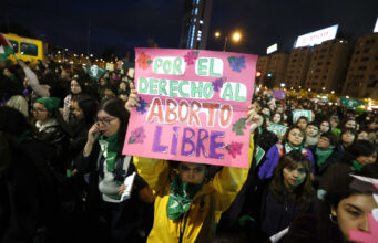 Protestas en Chile contra ley de latidos fetales y aborto Manifestante sostiene un cartel rosa sobre el aborto libre durante una marcha nocturna en Chile.