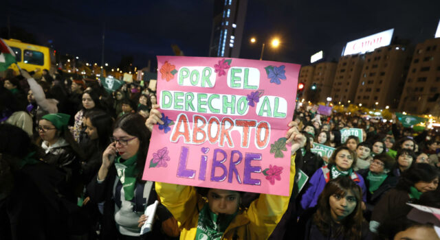 Protestas en Chile contra ley de latidos fetales y aborto Manifestante sostiene un cartel rosa sobre el aborto libre durante una marcha nocturna en Chile.