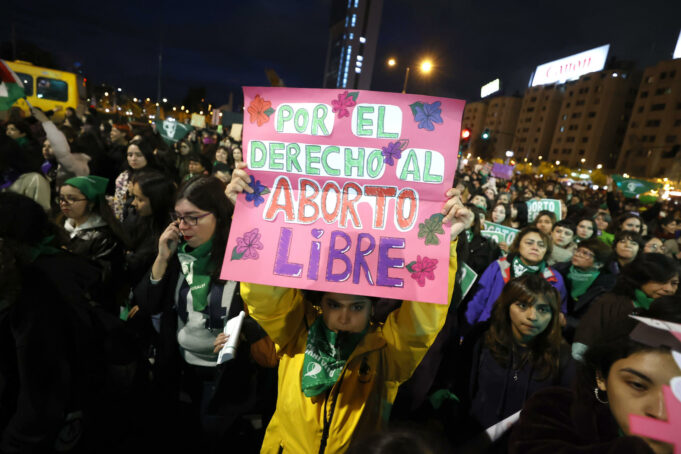 Protestas en Chile contra ley de latidos fetales y aborto Manifestante sostiene un cartel rosa sobre el aborto libre durante una marcha nocturna en Chile.