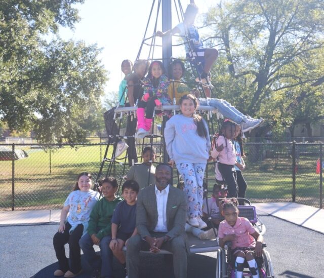 El alcalde Randall L. Woodfin posa junto a un grupo de niños en una estructura de juego de un parque en Birmingham.