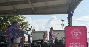 Renovación de City Lake Park en Russellville recibe impulso financiero Concierto en vivo "Jam on Sloss Lake" en el escenario de Russellville Alabama con cartel rosa de T-Mobile Hometown Grant.
