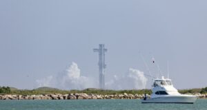 SpaceX cancela el lanzamiento número 13 de Starship Torre de lanzamiento de Starship rodeada de humo blanco con un yate navegando en primer plano en Texas.