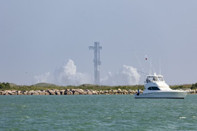 Torre de lanzamiento de Starship rodeada de humo blanco con un yate navegando en primer plano en Texas.