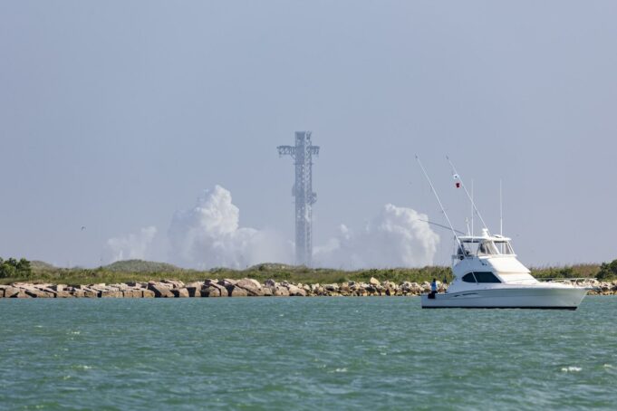 SpaceX cancela el lanzamiento número 13 de Starship Torre de lanzamiento de Starship rodeada de humo blanco con un yate navegando en primer plano en Texas.
