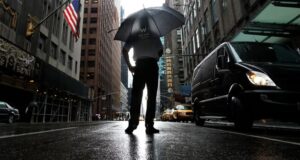 Tormentas severas en Nueva York amenazan con tornados Hombre con paraguas bajo fuertes lluvias y tormentas severas en una calle inundada de Nueva York.