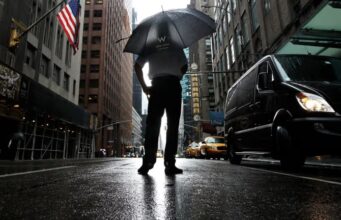Tormentas severas en Nueva York amenazan con tornados Hombre con paraguas bajo fuertes lluvias y tormentas severas en una calle inundada de Nueva York.