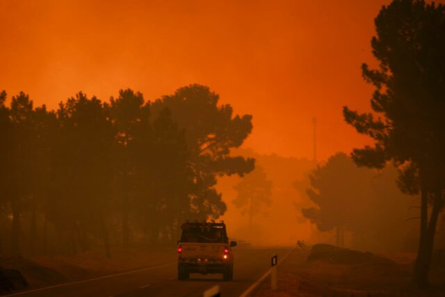 Vehículo de emergencia transitando por carretera rodeada de humo por incendio forestal en Portugal.