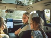 Vehículos eléctricos tendrán pruebas de manejo gratis Una madre sonríe a sus hijas desde el asiento delantero de un moderno vehículo eléctrico con techo panorámico de cristal.