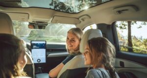 Vehículos eléctricos tendrán pruebas de manejo gratis Una madre sonríe a sus hijas desde el asiento delantero de un moderno vehículo eléctrico con techo panorámico de cristal.