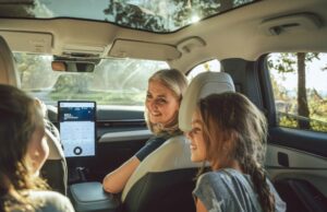 Vehículos eléctricos tendrán pruebas de manejo gratis Una madre sonríe a sus hijas desde el asiento delantero de un moderno vehículo eléctrico con techo panorámico de cristal.