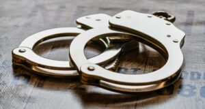 Arresto en Alabama de alumno por amenaza terrorista escolar Esposas metálicas de policía sobre una superficie de madera tras el arresto de un estudiante en Alabama.