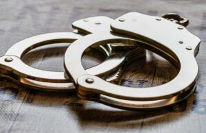 Arresto en Alabama de alumno por amenaza terrorista escolar Esposas metálicas de policía sobre una superficie de madera tras el arresto de un estudiante en Alabama.