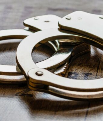 Arresto en Alabama de alumno por amenaza terrorista escolar Esposas metálicas de policía sobre una superficie de madera tras el arresto de un estudiante en Alabama.