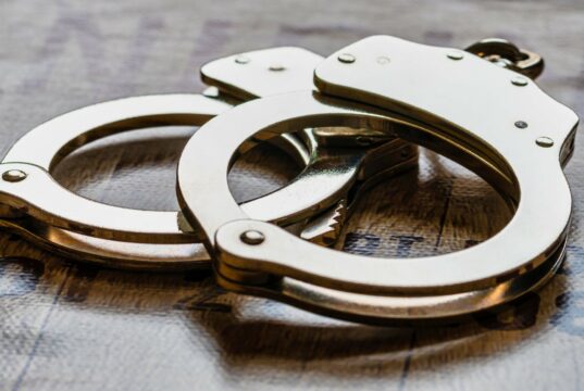 Arresto en Alabama de alumno por amenaza terrorista escolar Esposas metálicas de policía sobre una superficie de madera tras el arresto de un estudiante en Alabama.