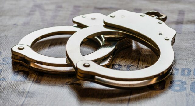 Arresto en Alabama de alumno por amenaza terrorista escolar Esposas metálicas de policía sobre una superficie de madera tras el arresto de un estudiante en Alabama.