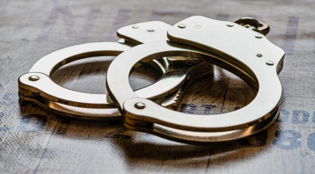 Esposas metálicas de policía sobre una superficie de madera tras el arresto de un estudiante en Alabama.