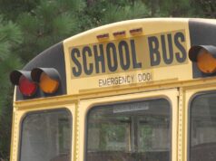 Escasez de conductores causa retrasos en autobuses escolares Parte trasera superior de un autobús escolar amarillo con las letras School Bus y luces de advertencia.