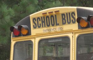 Escasez de conductores causa retrasos en autobuses escolares Parte trasera superior de un autobús escolar amarillo con las letras School Bus y luces de advertencia.