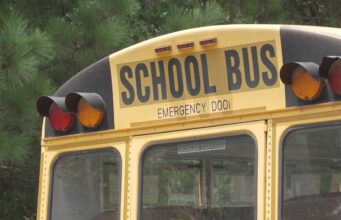 Escasez de conductores causa retrasos en autobuses escolares Parte trasera superior de un autobús escolar amarillo con las letras School Bus y luces de advertencia.