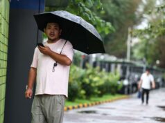 China declara alertas rojas por lluvias e inundaciones Hombre en China sosteniendo un paraguas negro bajo la lluvia mientras mira su teléfono móvil.